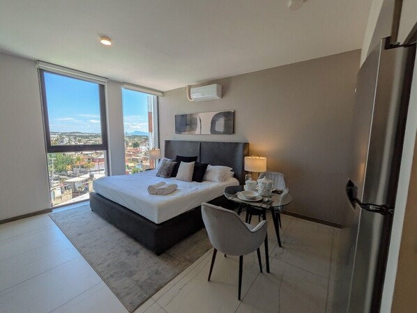 A modern hotel room with a large bed, a dining table, and a view of the city.
