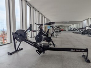 Une salle de sport équipée de vélos d’appartement, d’un rameur et de tapis de course.