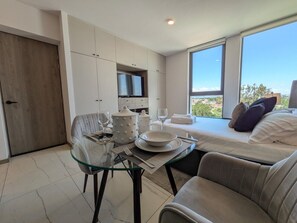 Ein modernes Schlafzimmer mit Bett, einem Glastisch mit Esstisch-Set und einem an der Wand montierten Fernseher.