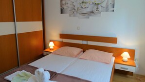 Una cama bien hecha con dos almohadas, una mesita de noche con una lámpara y una obra de arte floral colgada en la pared.