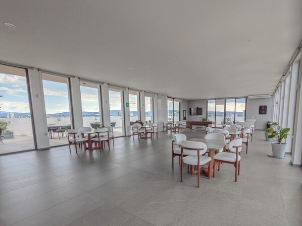 A spacious indoor area with multiple seating arrangements, large windows, and a view of the outside.