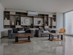 A modern living room with two sofas, a coffee table, and a side table. There are shelves with decorative items and an air conditioning unit on the wall. - Amazing new apartment near Andares 1209B (Zapopan)