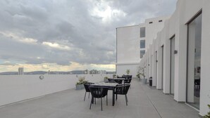 A rooftop terrace with a table and chairs, a view of the city skyline, and a modern building with large windows.
