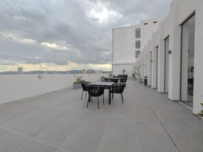 A rooftop terrace with a table and chairs, a view of the city skyline, and a modern building with large windows. - Amazing new apartment near Andares 1209B (Zapopan)