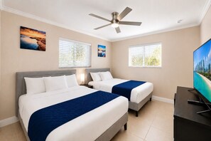 A hotel room with two beds, a ceiling fan, a television, and artwork on the walls.