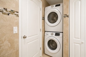 A laundry room with two stacked front-loading washing machines, a white door, and a tiled wall.