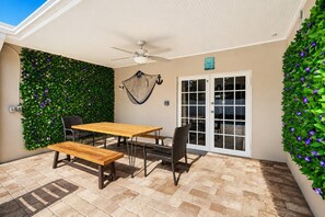 Une terrasse avec une table et des chaises, un ventilateur de plafond et un mur recouvert de feuillage verdoyant.