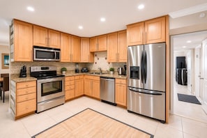 A modern kitchen with wooden cabinets, stainless steel appliances, and a tiled floor.