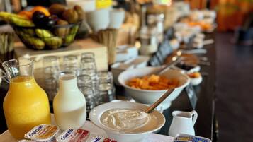 A buffet table with various food items and beverages, including Danone yogurt, fruits, and a bowl of mixed fruits.
