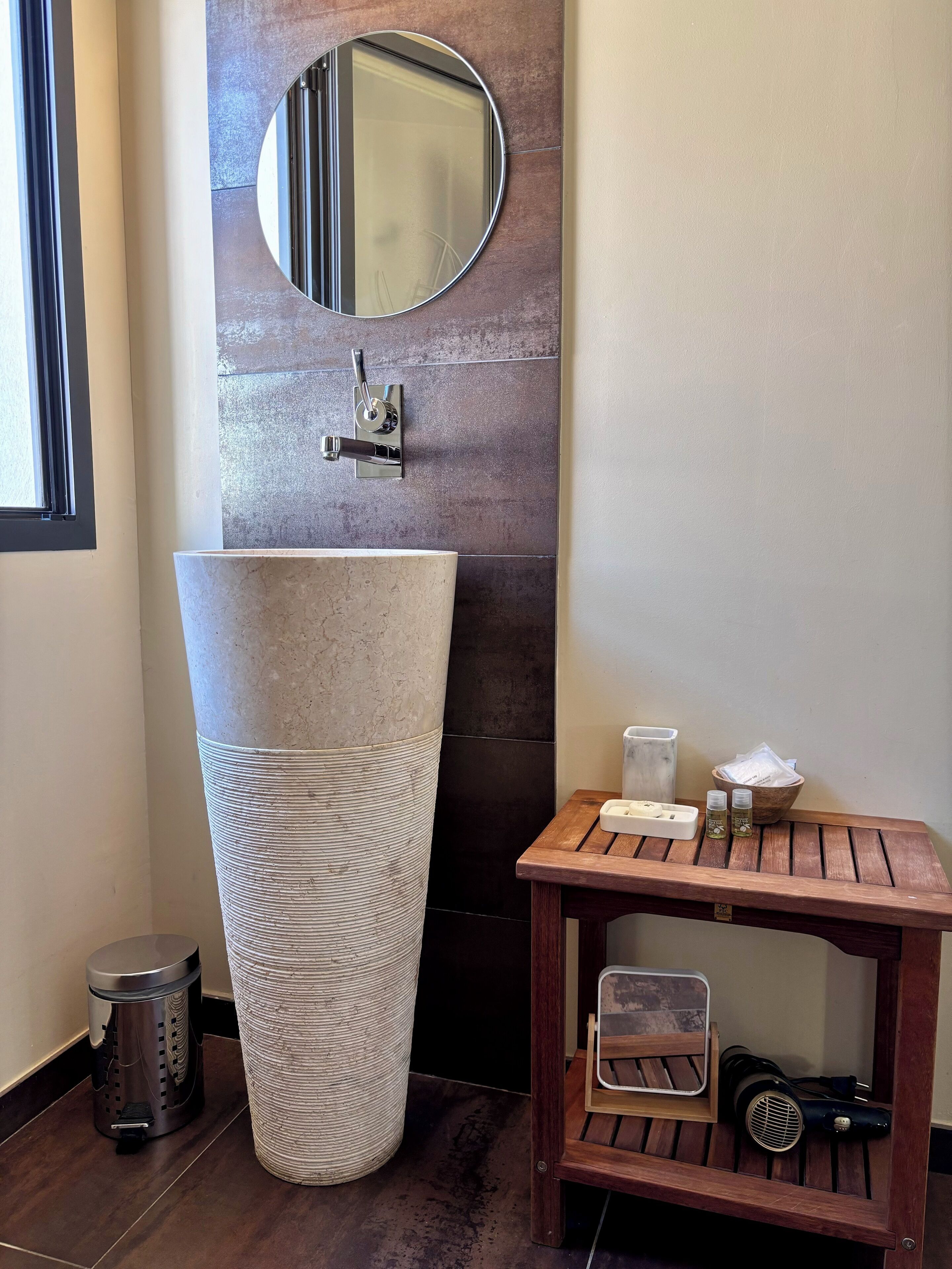 Een badkamer met een grote wastafel, een ronde spiegel, een houten wastafelmeubel en een haardroger.