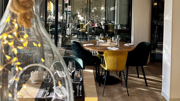 A modern dining area with a round table, yellow chairs, and a glass bottle centerpiece. - Hotel Restaurant Le Vinois (Caillac)