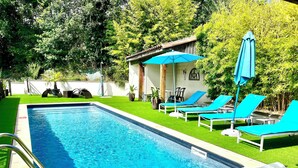A rectangular swimming pool with a metal ladder, surrounded by green artificial grass and blue lounge chairs with umbrellas. - Hotel Restaurant Le Vinois (Caillac)