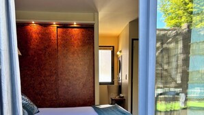 A bedroom with a large bed, a window with a view of a tree, and a sliding glass door leading to an outdoor area. - Hotel Restaurant Le Vinois (Caillac)