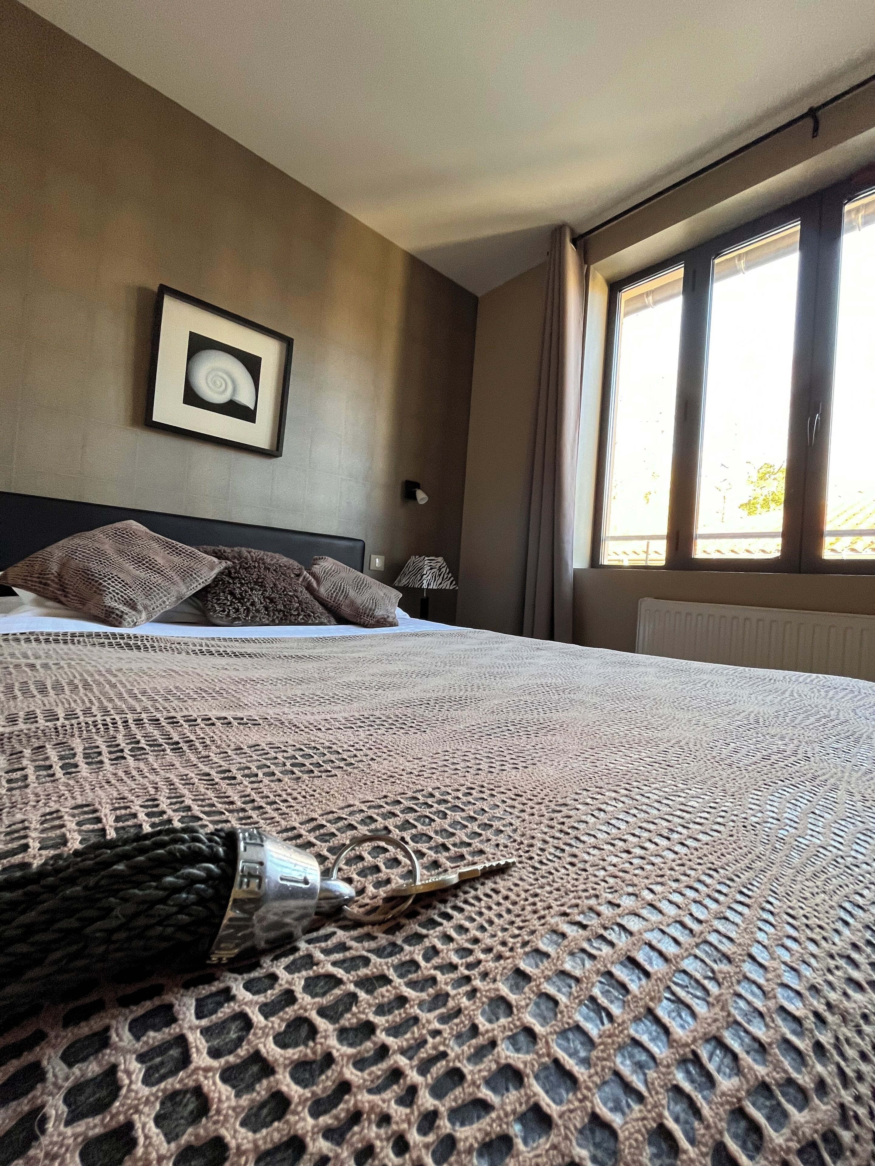 Een hotelkamer met een groot bed, een ingelijst kunstwerk aan de muur en een raam met gordijnen.