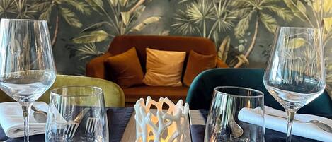 Une table à manger dressée avec de la vaisselle transparente, un chandelier blanc et, en arrière-plan, un mur orné d’un motif de feuilles tropicales.