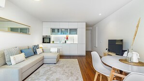 A modern living room with a sofa, a dining table, and a kitchen area with white cabinets and appliances. - Bombarda Patio Oasis by LovelyStay (Porto)
