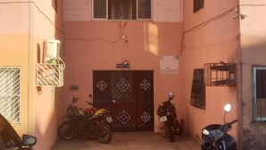 Un immeuble résidentiel doté d’une entrée sécurisée par un portail, avec deux motos garées devant et un cône de signalisation sur le trottoir.