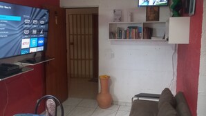 Un salon avec un téléviseur, un ventilateur de plafond, un canapé, une table et un vase.