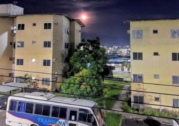 A building with multiple windows and balconies, a parked bus in front, and a tree in the foreground. - Victor Inn - (Manaus)