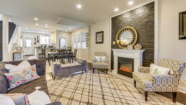 A spacious living room with a fireplace, patterned armchairs, and a dining area in the background. - 6 Mi to Downtown - Spacious Home in Pittsburgh! (Pittsburgh)