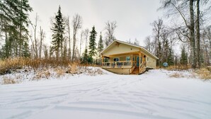 Eine Hütte mit Veranda, umgeben von Schnee und Bäumen.