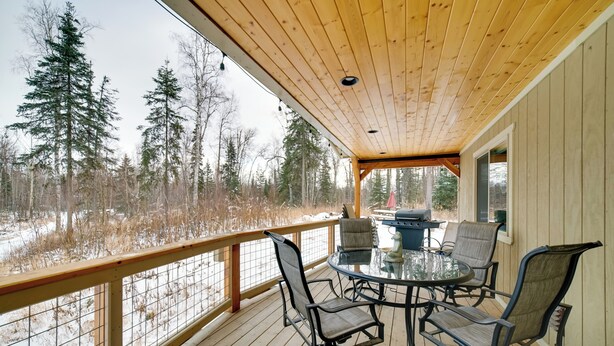 Eine Holzterrasse mit einem Glastisch und Stühlen mit Blick auf eine verschneite Landschaft mit Bäumen.