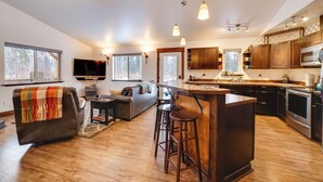 Eine moderne Küche mit Holzschränken, einer zentralen Kochinsel mit Barhocker und einem Essbereich mit Sofa und Couchtisch.