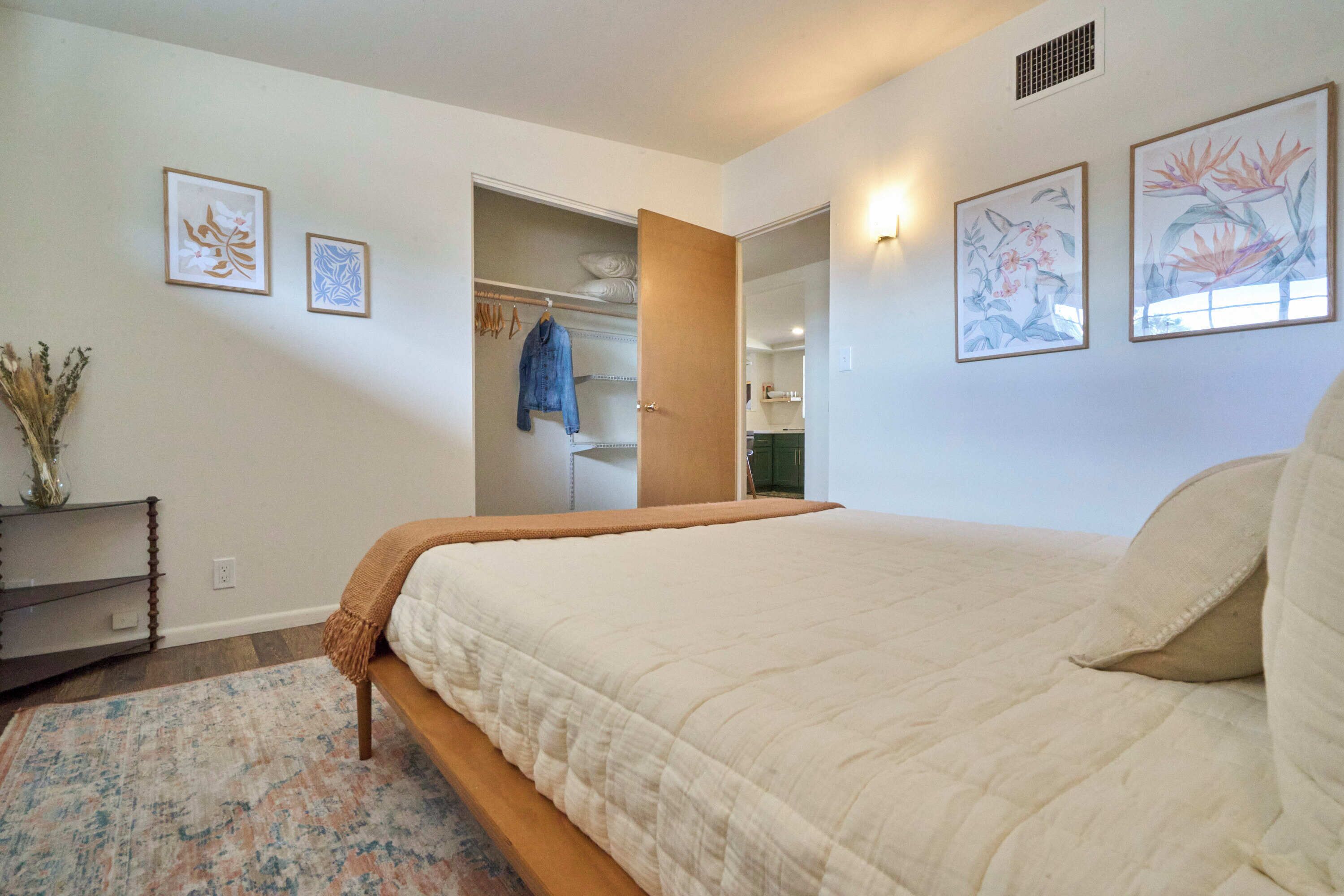 Um quarto com cama, mesa de cabeceira, cômoda e armário.