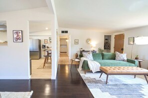 A modern living room with a green sofa, a wooden coffee table, and a dining area with a kitchen in the background. - Spacious Living •Fully Stocked Kitchen •Private Yard •Pets Welcome •12 min to DT (Tucson)