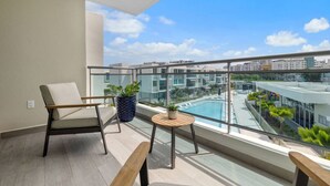 A balcony with a view of a swimming pool, a chair, a small table, and a potted plant. - Poolfront penthouse by beach (Carolina)
