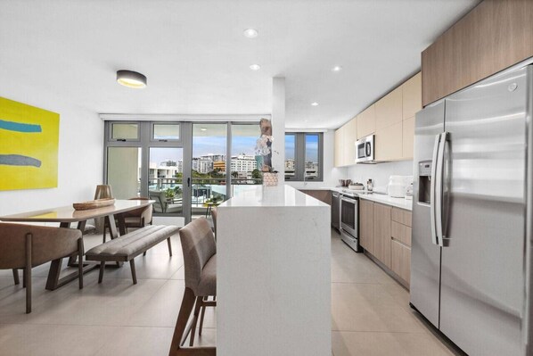 A modern kitchen with a central island, stainless steel appliances, and a dining area with benches.