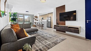 A modern living room with a grey sofa, a patterned rug, and a flat-screen TV mounted on a wall. - Poolfront penthouse by beach (Carolina)