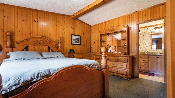 Een slaapkamer met houten lambrisering, een groot bed, een kapstok en een spiegel.