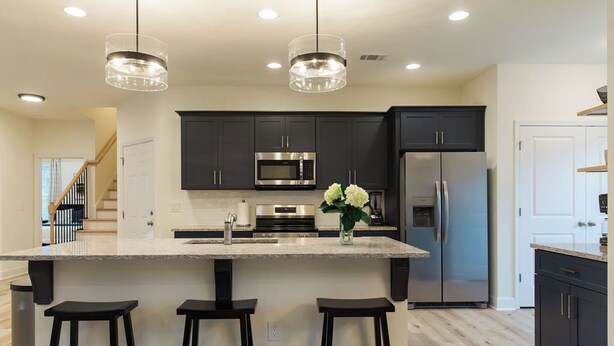 A modern kitchen with dark cabinets, stainless steel appliances, and a central island with stools.