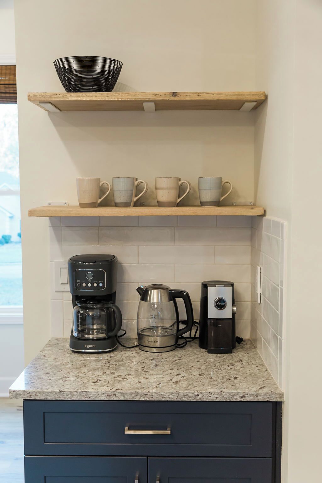 A kitchen with a coffee maker, a kettle, and a mug on the counter. There are two wooden shelves above the counter.