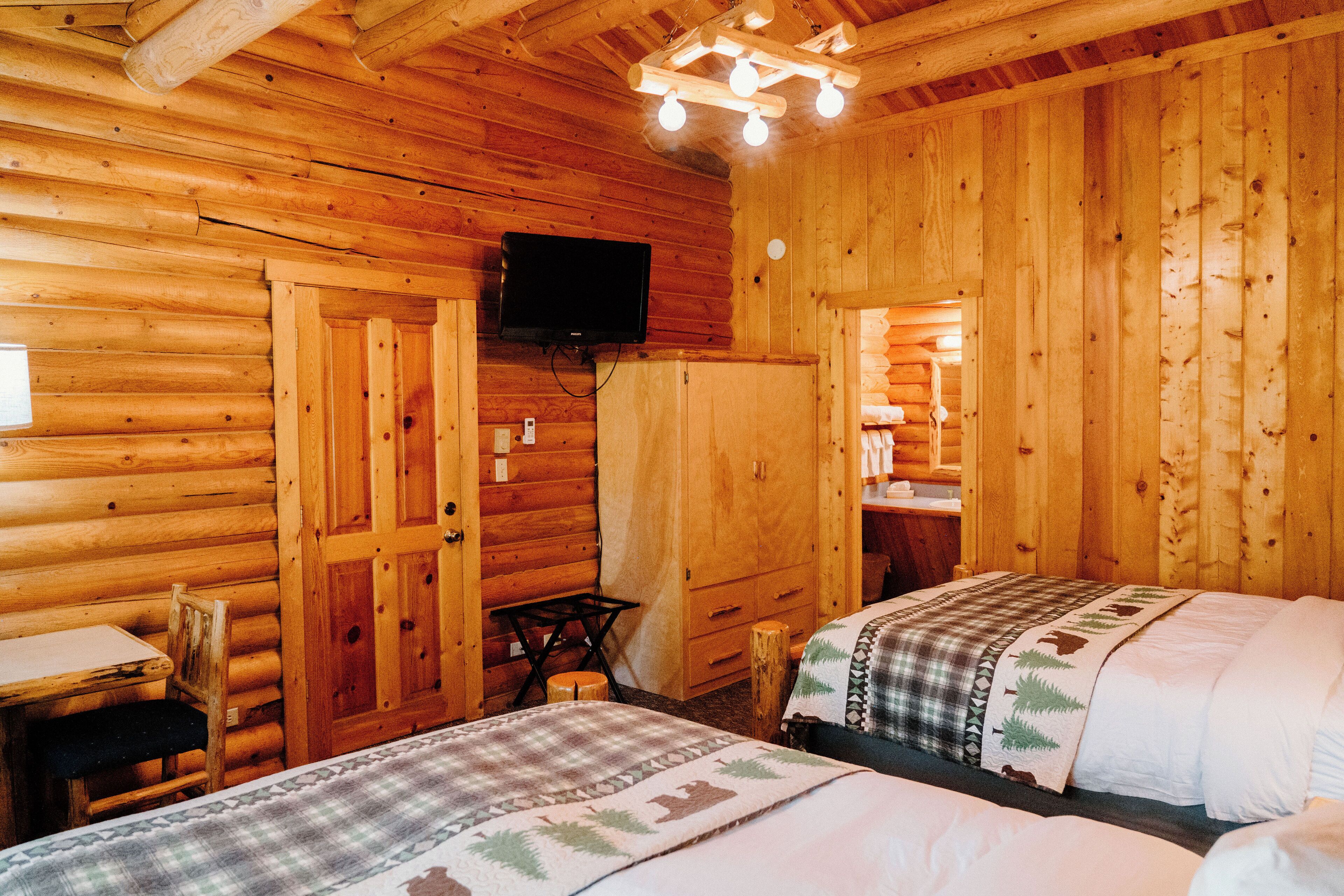 A wooden cabin room with two beds, a TV, a table, and a chair.