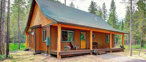 A log cabin with a porch, large windows, and a chimney.