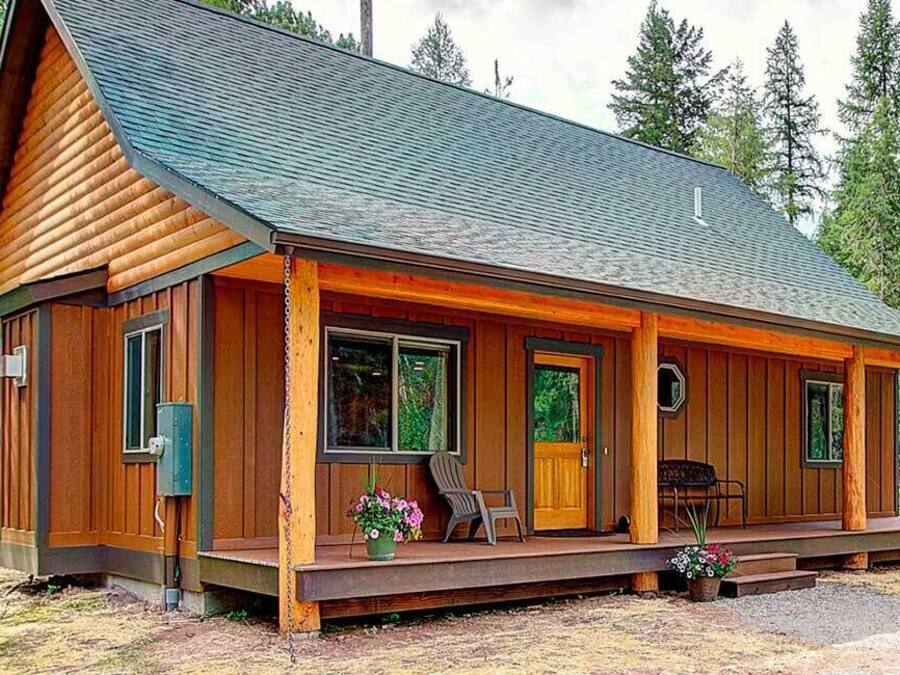 Una cabaña de troncos con un porche, ventanas grandes y una chimenea.