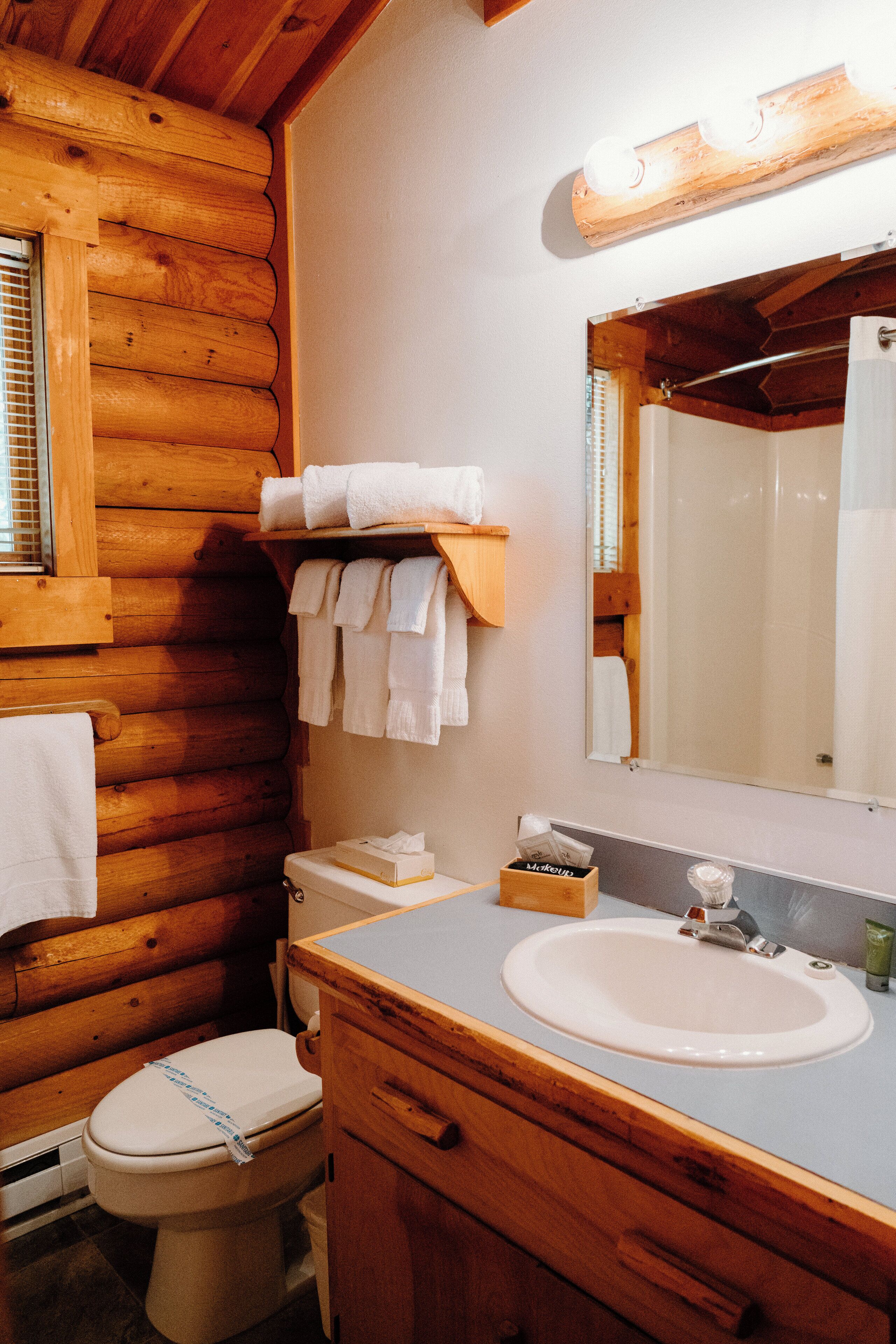 A wooden cabin bathroom with a toilet, sink, and mirror.