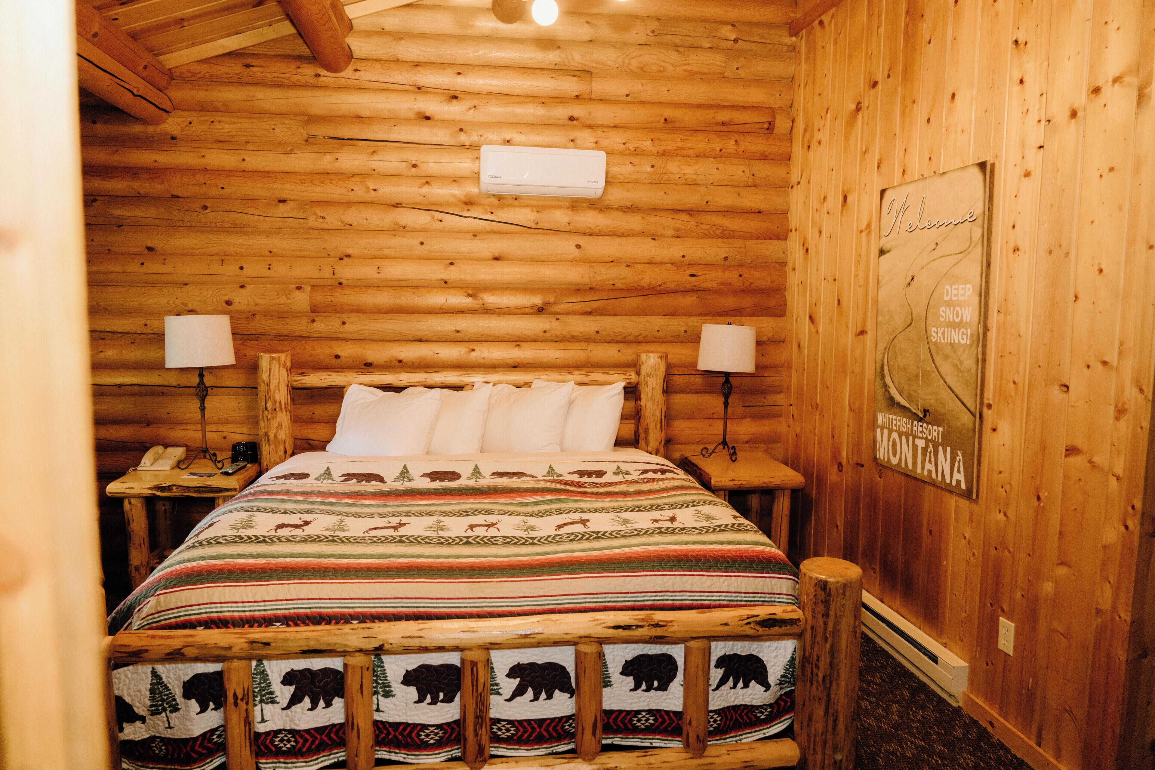 Une chambre dans un chalet en bois, avec un lit, deux lampes de chevet, un téléphone et une pancarte de bienvenue.