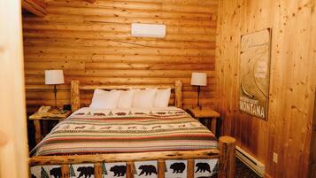 Una habitación tipo cabaña de madera con una cama, dos lámparas de noche, un teléfono y un cartel de bienvenida.