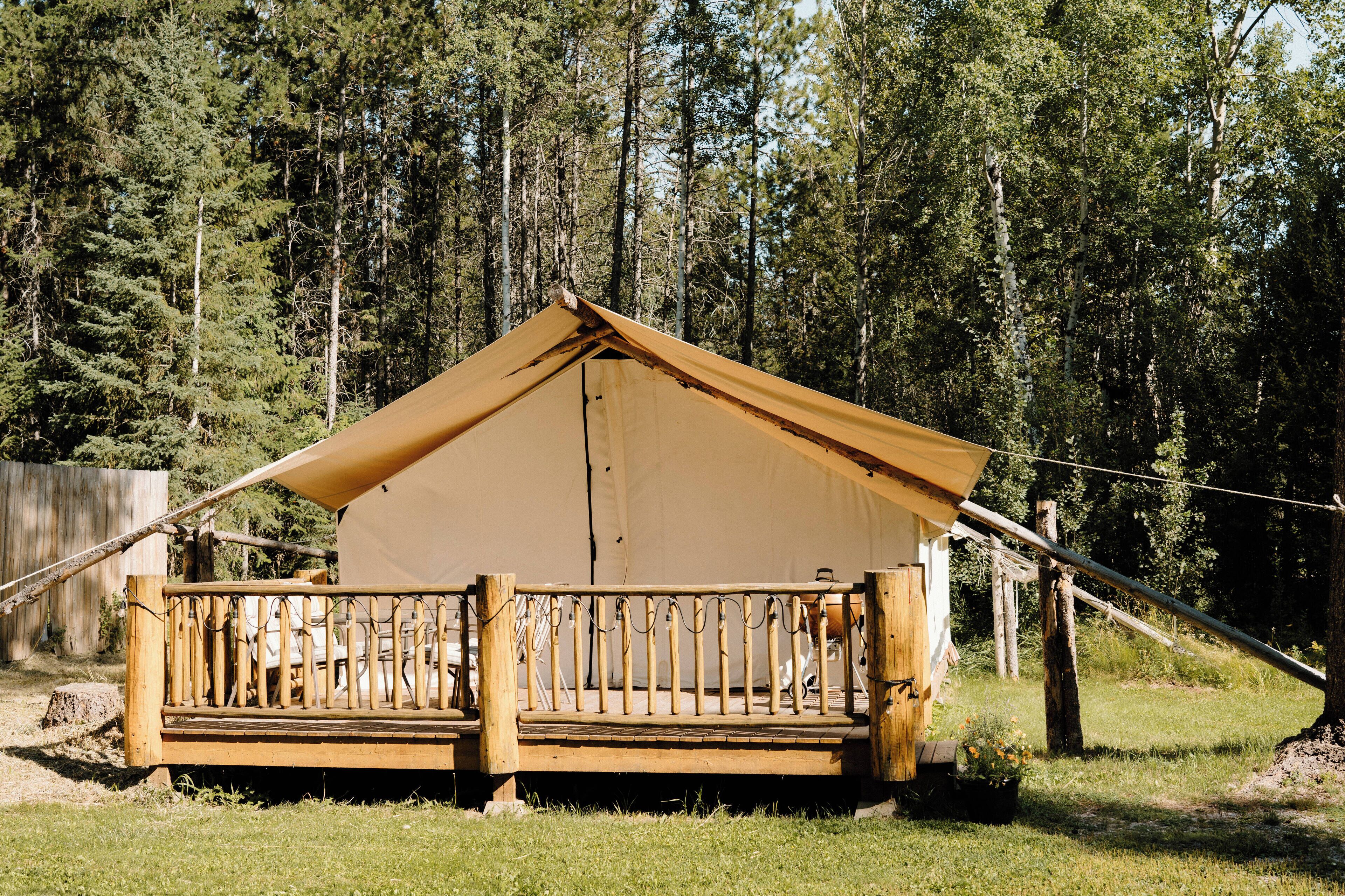 A tent with a wooden deck and railing, surrounded by a forest.