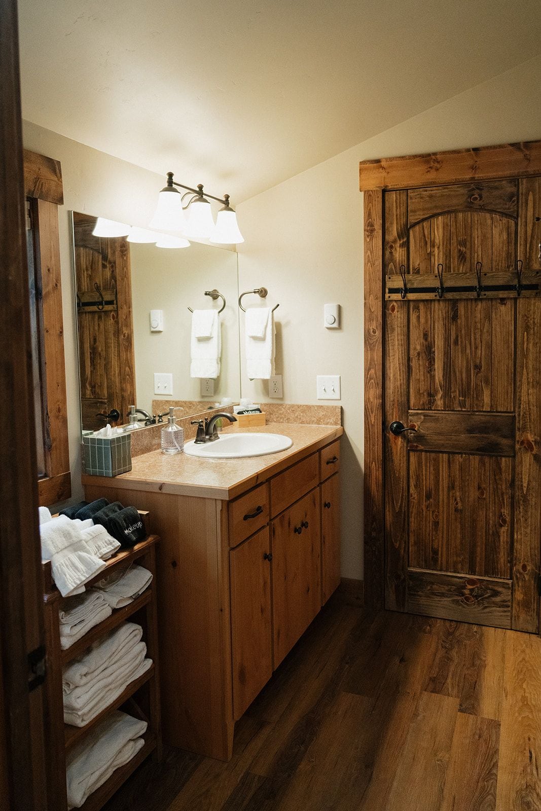 A bathroom with a wooden door, a sink with a mirror, and a towel rack.
