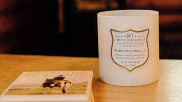 A white candle labeled "MI Manly Indulgence Warm Beachwood" and a stack of books on a wooden surface.