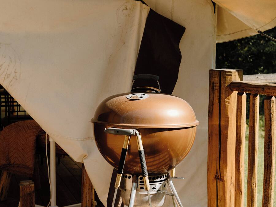 Una parrilla portátil de barbacoa sobre una terraza de madera bajo una carpa.