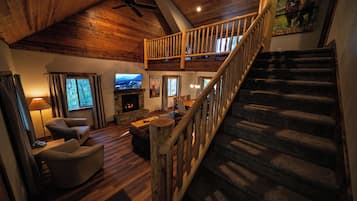 Amplia sala de estar con chimenea, asientos cómodos, televisor y una escalera que lleva a un nivel superior.