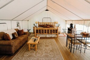 Un alloggio in tenda con un letto di legno, un divano, un tavolo da pranzo e sedie.
