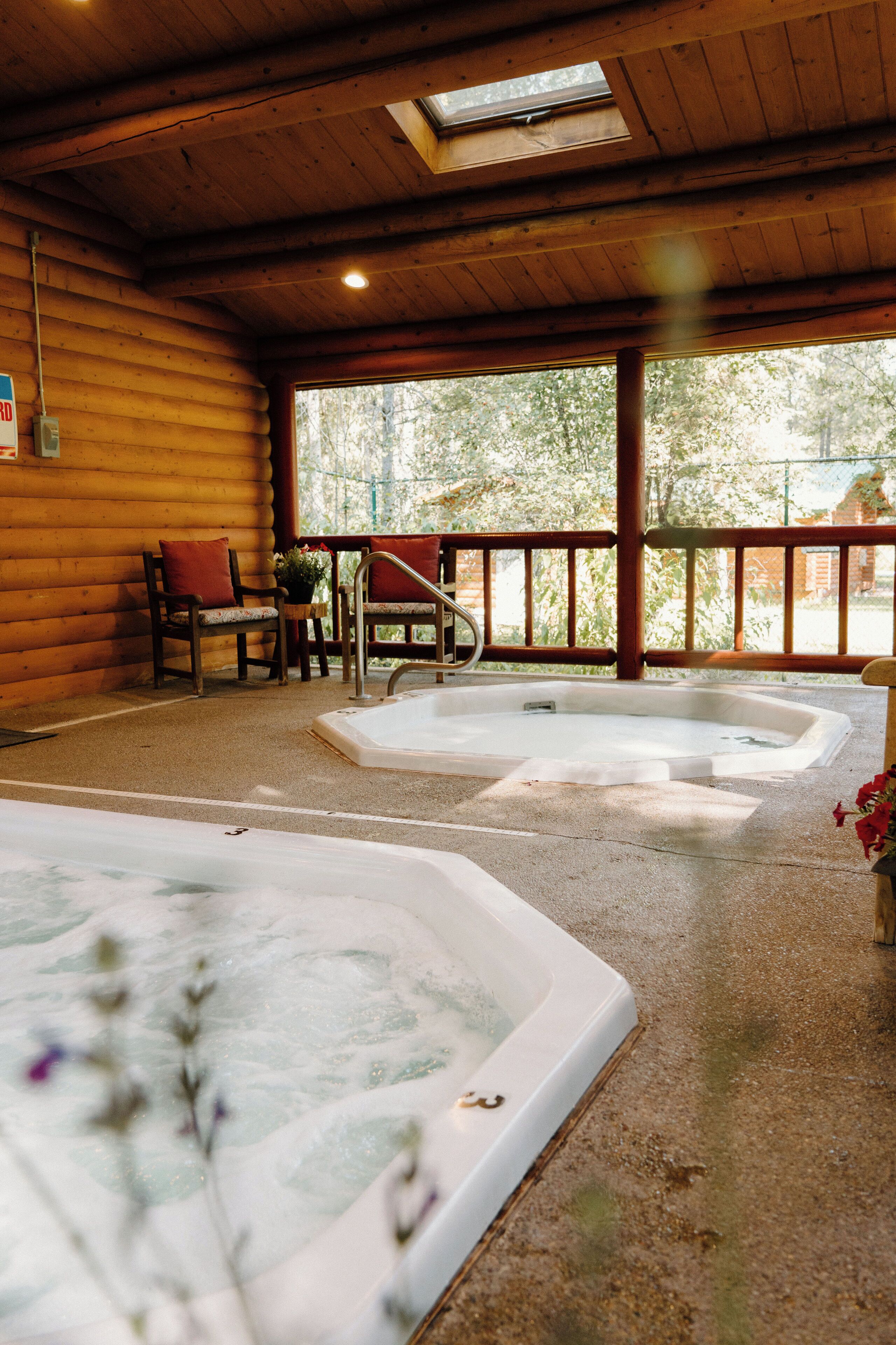 A wooden cabin with two hot tubs and a seating area with chairs and a table.