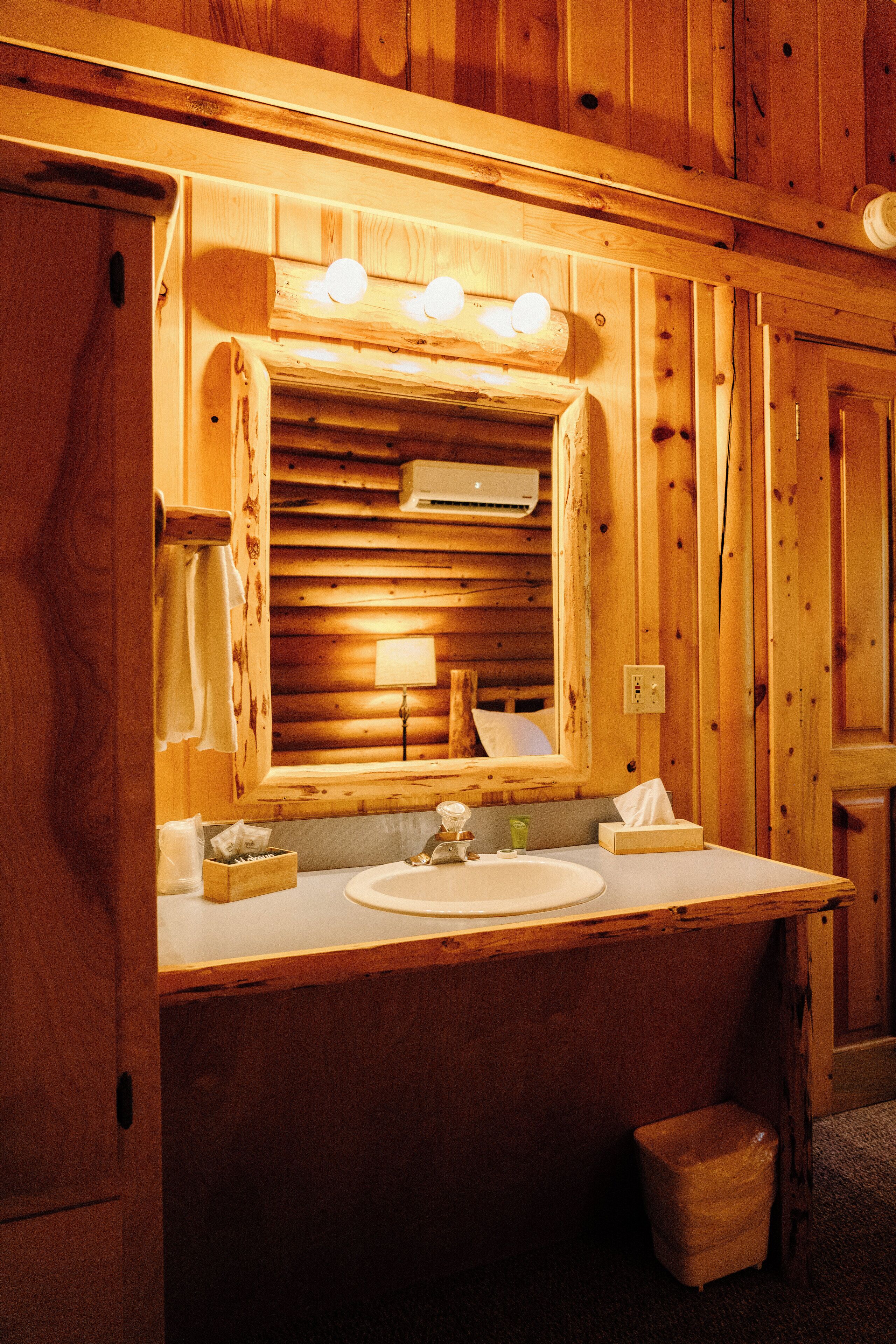 A wooden cabin-style bathroom with a sink, mirror, and towel rack.