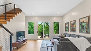 A modern living room with a staircase, a sofa, a coffee table, and a TV. - Mtn View, 3 Miles to DT AVL, King Bed, Fire Pit (Asheville)